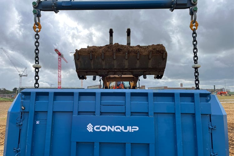 A telehandler with a large bucket putting mud into a large blue BulkX skip. The word Conquip is written on the side.