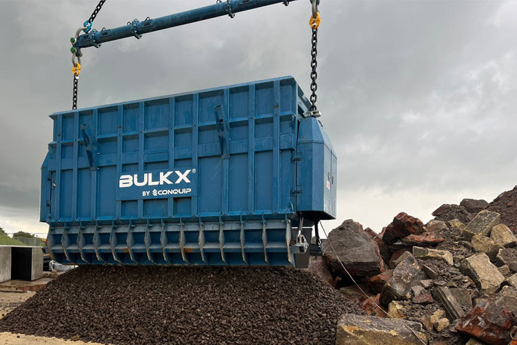 A large blue container with BulkX by Conquip on the side dropping large quantities of soil.
