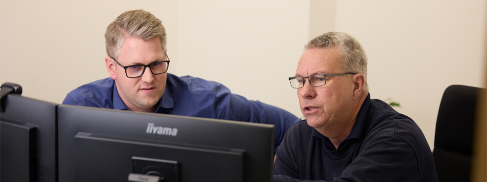 Two men at a table looking at a computer.