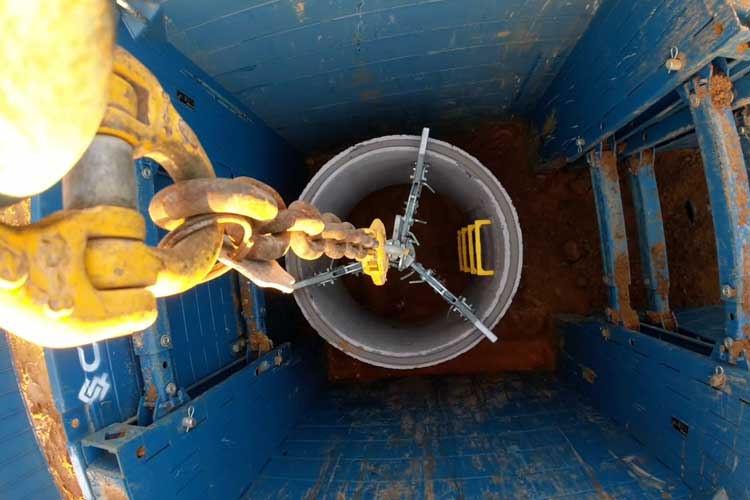A Conquip Manhole Box with a Concrete pipe being dropped into a hole by a Mechanical Manhole Ring Lifter.