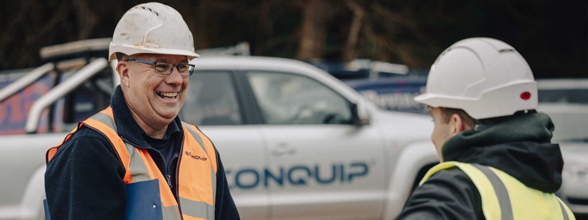 Two men talking in front of a Conquip Pick-up truck