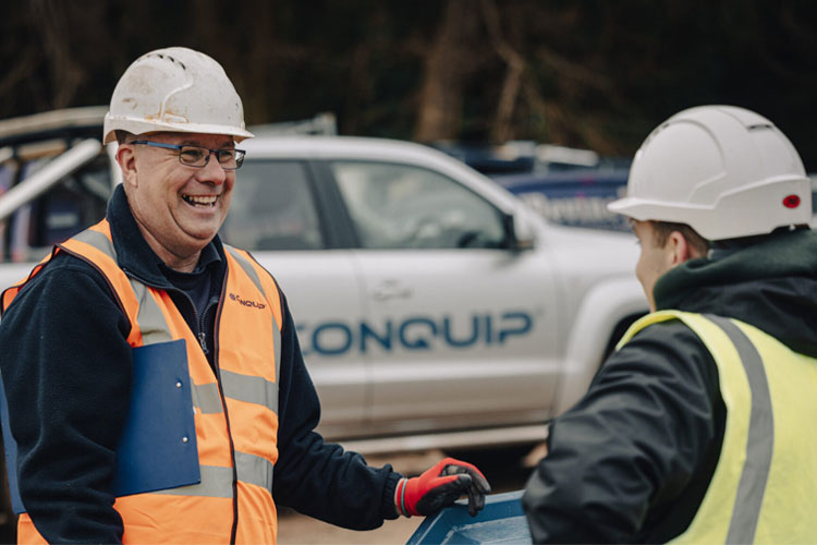 Two men talking in front of a Conquip Pick-up truck