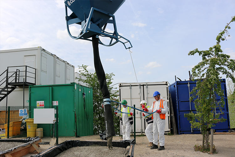 A Conquip Concrete Skip without Bale Arm being controlled by 2 men in high vis jackets