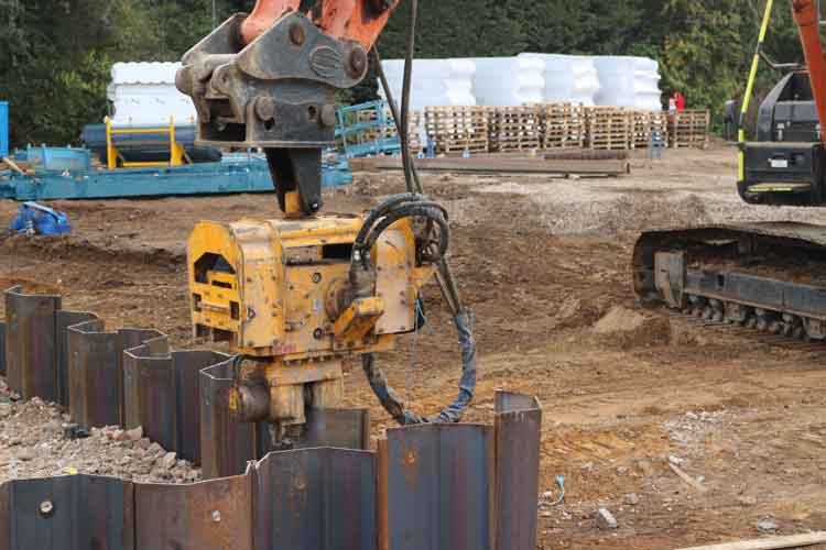 An excavator with an EV Hammer removing pile sheets around an excavation.