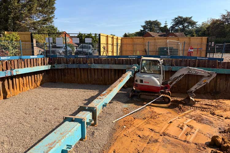 An excavation with an excavator in the middle with a brace holding the ground together in the middle.